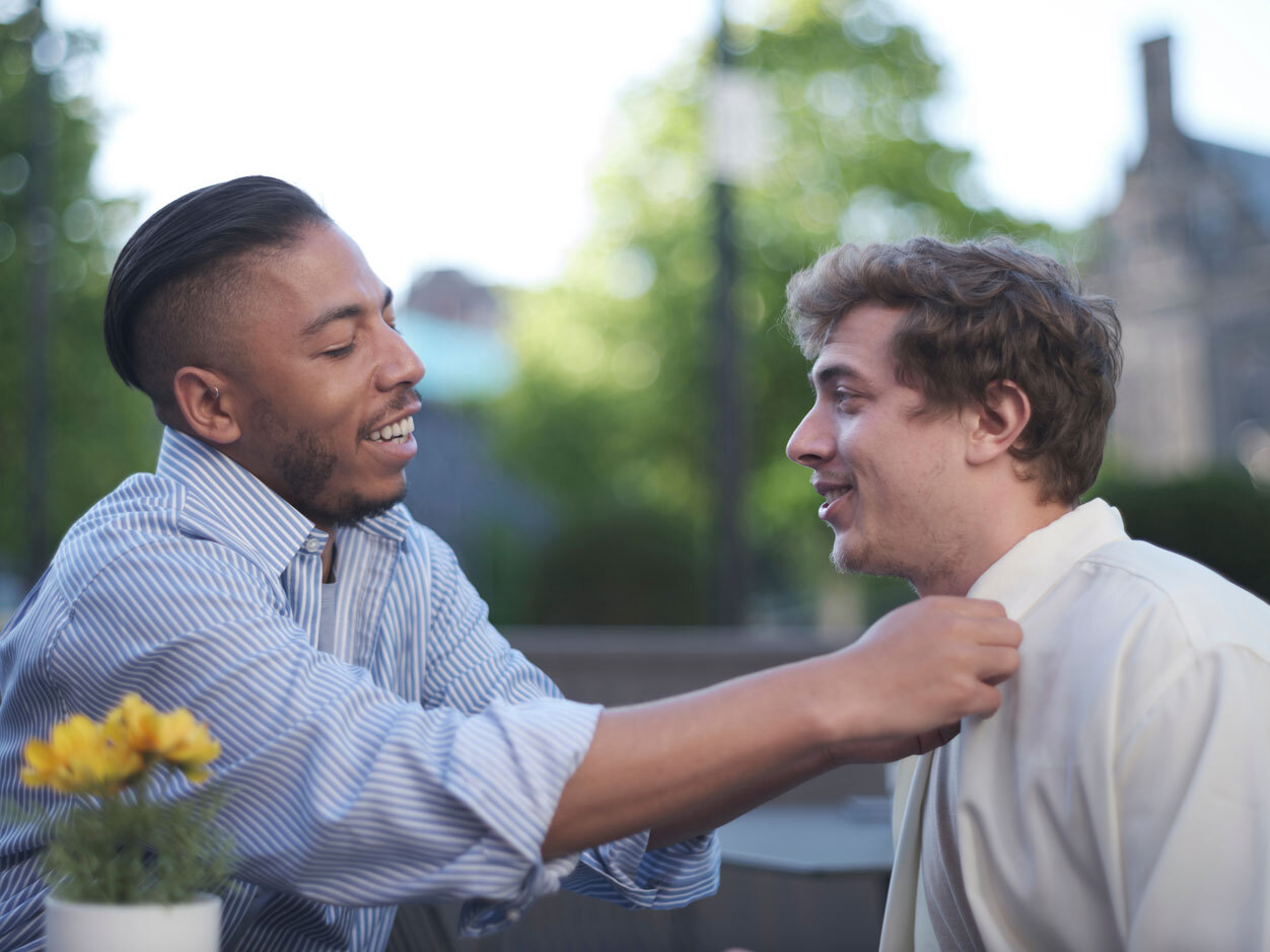 One man helps another man to adjust his shirt.
