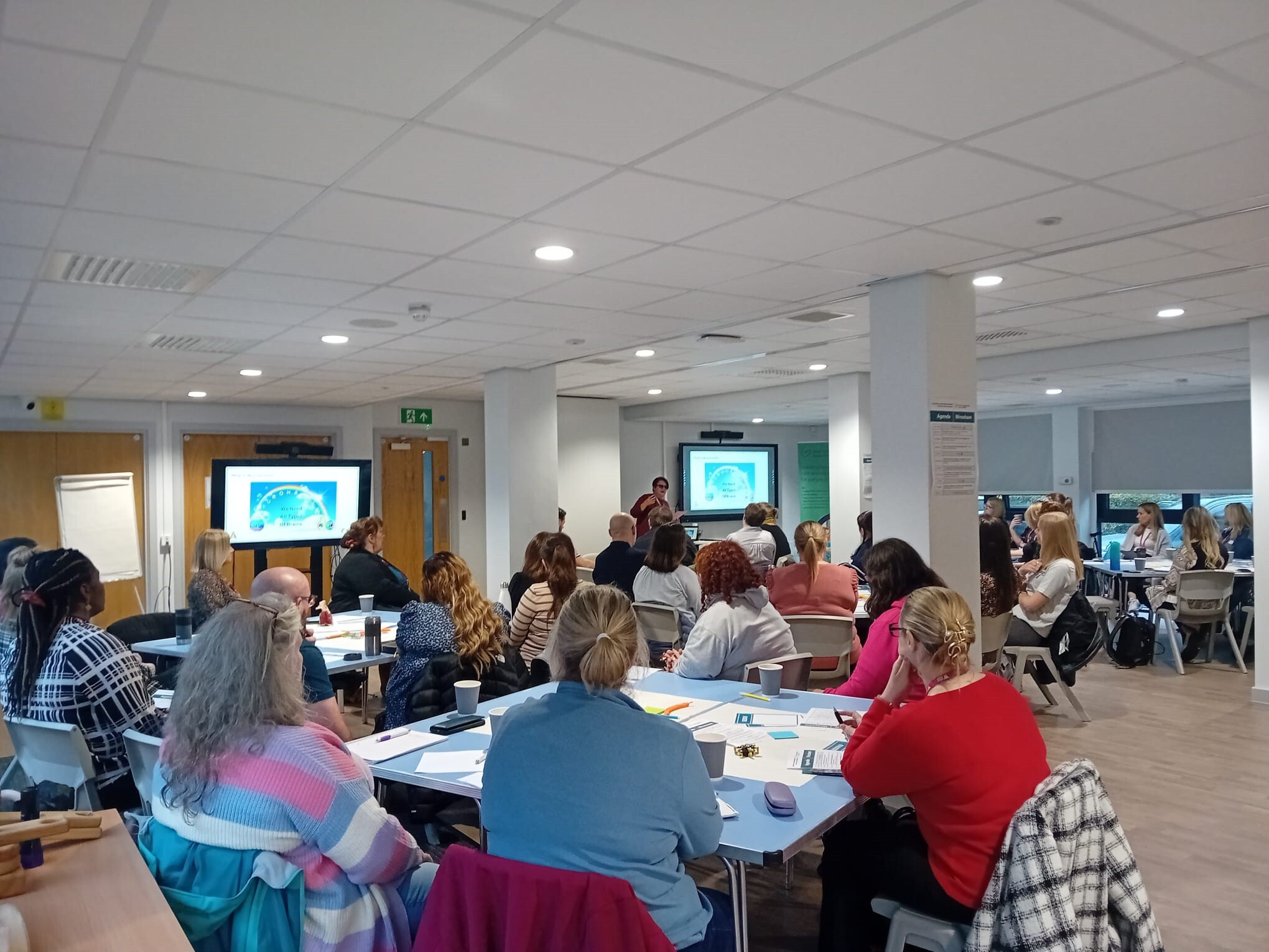 People in a conference setting looking at screens and a speaker